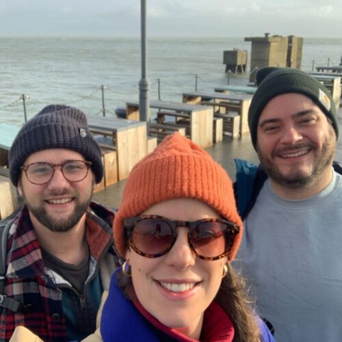 A selfie of 3 people smiling to camera on Folkestone harbour with the sea in the background.