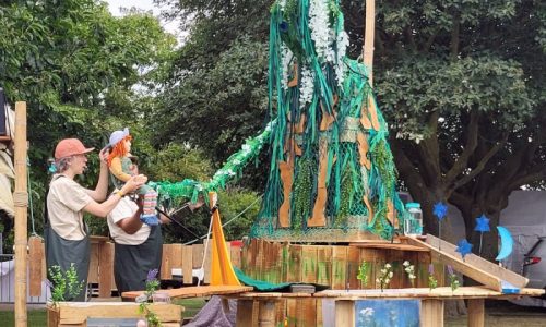 Lyra sits on the hand of Old Mother River, a giant willow tree puppet