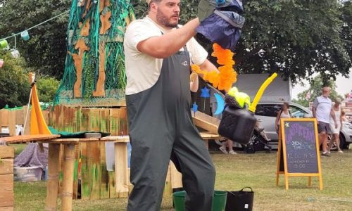 A litter monster puppet stands over his mess of multicoloured plastic bottles